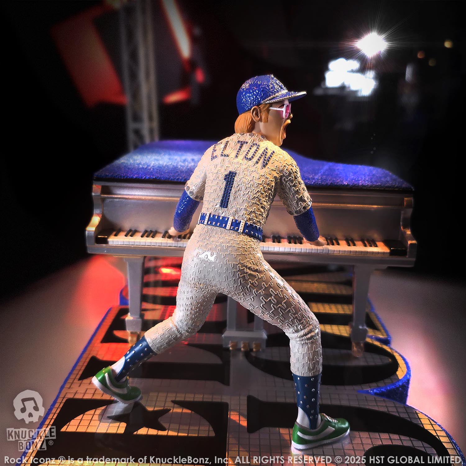 Statue of Elton John with a grand piano in a baseball uniform with 'Elton' on the back, on a stage with lights.