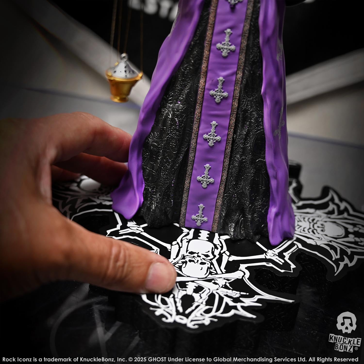 Hand holding a Statue of Papa V Perpetua from Ghost with purple accents and intricate design on a black and white patterned surface.
