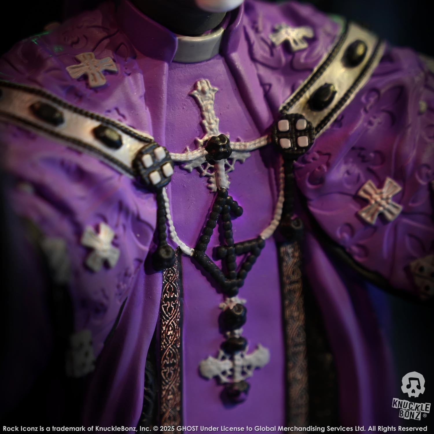 Close-up of a purple robe with cross designs and a detailed necklace on a dark background.