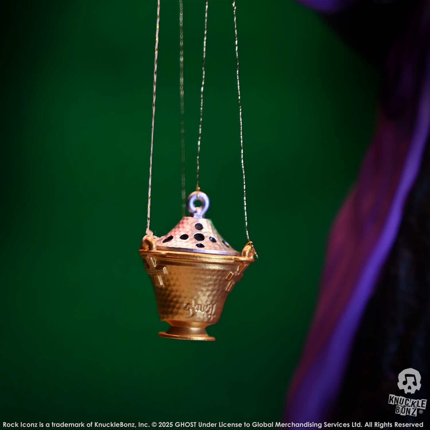 Gold incense burner hanging against a green background